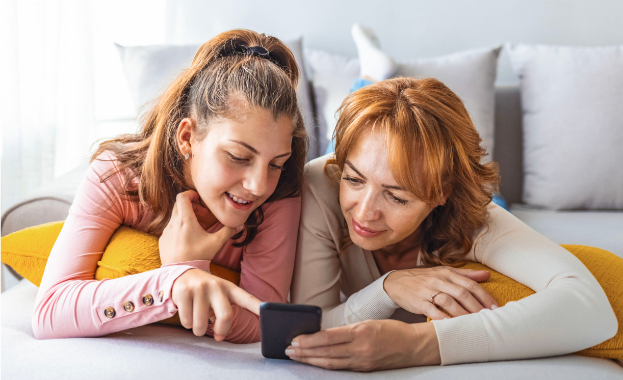 A mother and her daughter looking at a phone while lounging on a couch
