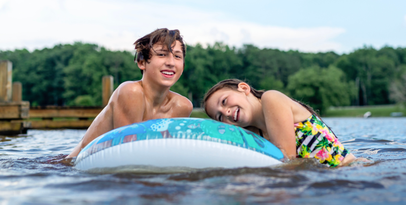 A young boy and a young girl holding onto a pool float outdoors in a body of water