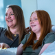 Aubri, a TZIELD® (teplizumab-mzwv) patient, smiling and sitting on the couch eating popcorn with her mother and caregiver, Molly